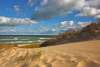 Sandy dunes with beach grass in the foreground and Lake Michigan visible under a partly cloudy sky at Indiana Dunes