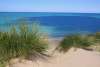 Beach grass on a sand dune framing a view of bright blue Lake Michigan water and clear sky at Indiana Dunes