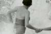Vintage black-and-white photograph of a person wading through crashing waves while holding another person's hand.