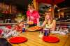 A waiter in a red shirt serves pizza to two young girls