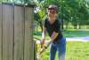 Woman washes hands with a hose connected to a well in a wooden enclosure.