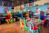 Colorful chairs, booths, and table are inside a restaurant. A mural and television are in the background.