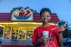A young boy eats a shake in front of an ice cream stand.