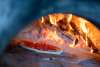 A pizza sits in a brick oven in front of logs that are aflame.