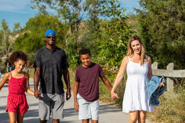 A family of four holds hands as they walk along a paved path through the dunes.