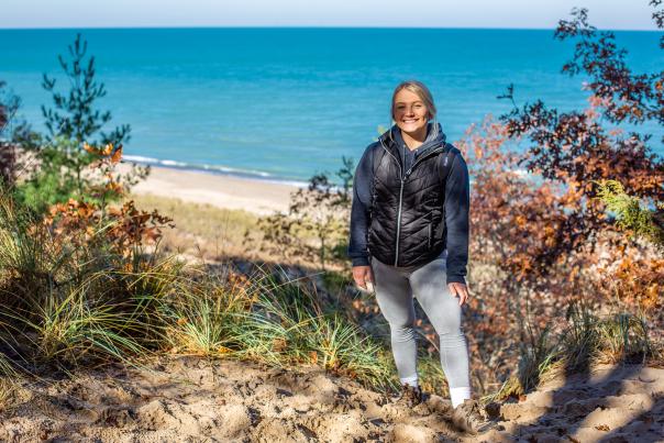Woman standing on a trail surrounded by fall foliage with Lake Michigan visible in the background at Indiana Dunes