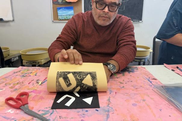 A man in a red sweater holds up a printed paper showing black and white abstract geometric art in a studio.