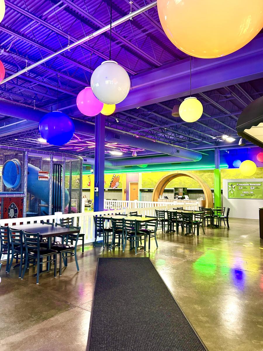 Indoor play area with colorful hanging sphere lights, tables, chairs, and a purple ceiling.