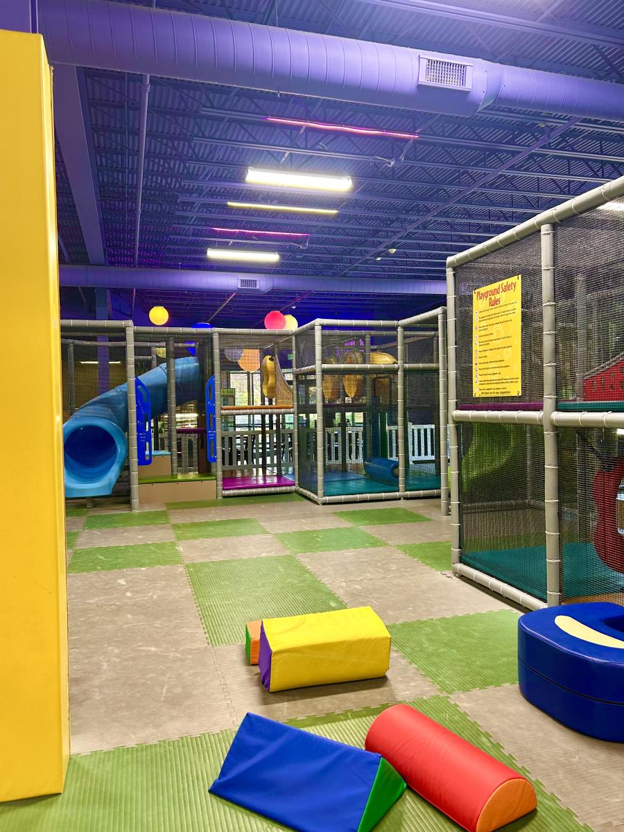 Indoor children's playground with climbing structures, a blue tube slide, and soft play mats.