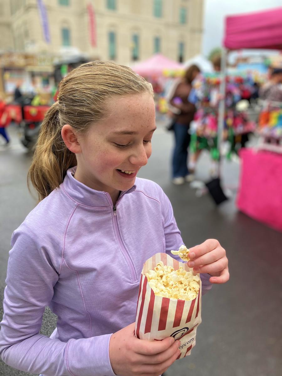 A young girl walks down the street while holding a bag of popcorn