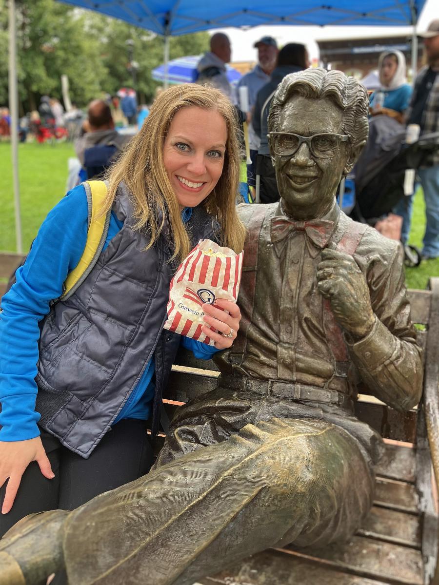 A woman sits next to a statue of Orville Rednebacher