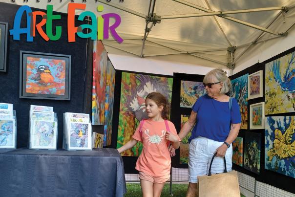 A woman and young child peruse art in a tent filled with art hanging on the wall.