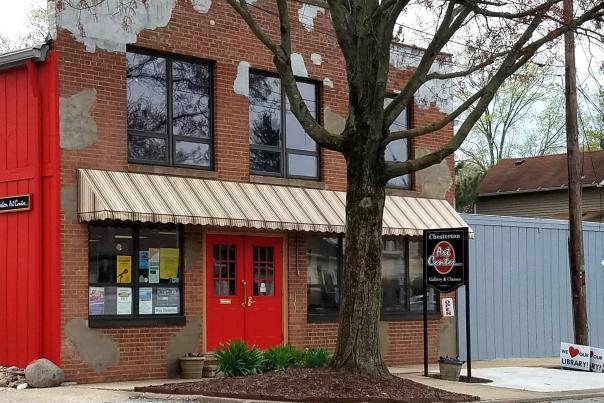 A brick building with a bright red door. A large tree sits in front of the building.