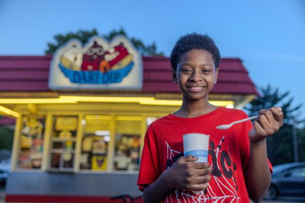 A young boy eats a shake in front of an ice cream stand.