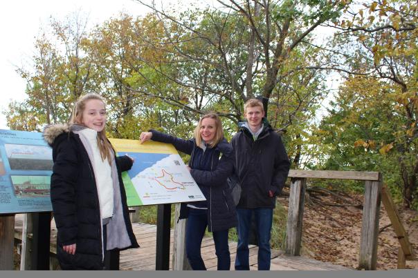 Three people in fall jackets pose next to a sign with trees in the background