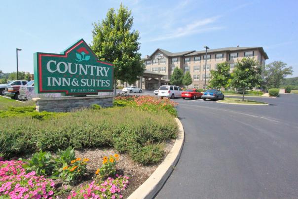 A sign with landscaping around it sits near a driveway. In the background is a hotel with cars parked in front.