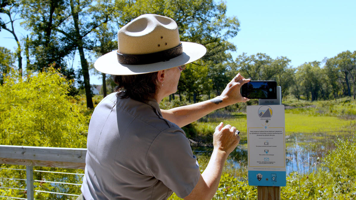 A park ranger puts her phone on a stand to take a picture of the landscape