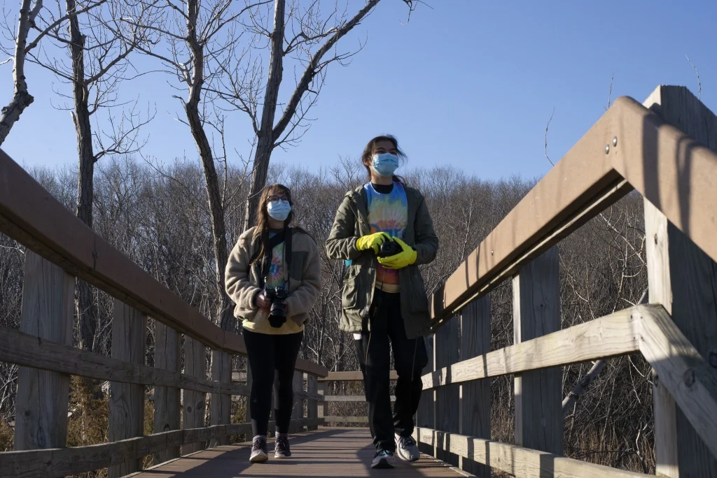 Two masked people walking on a dune boardwalk trail