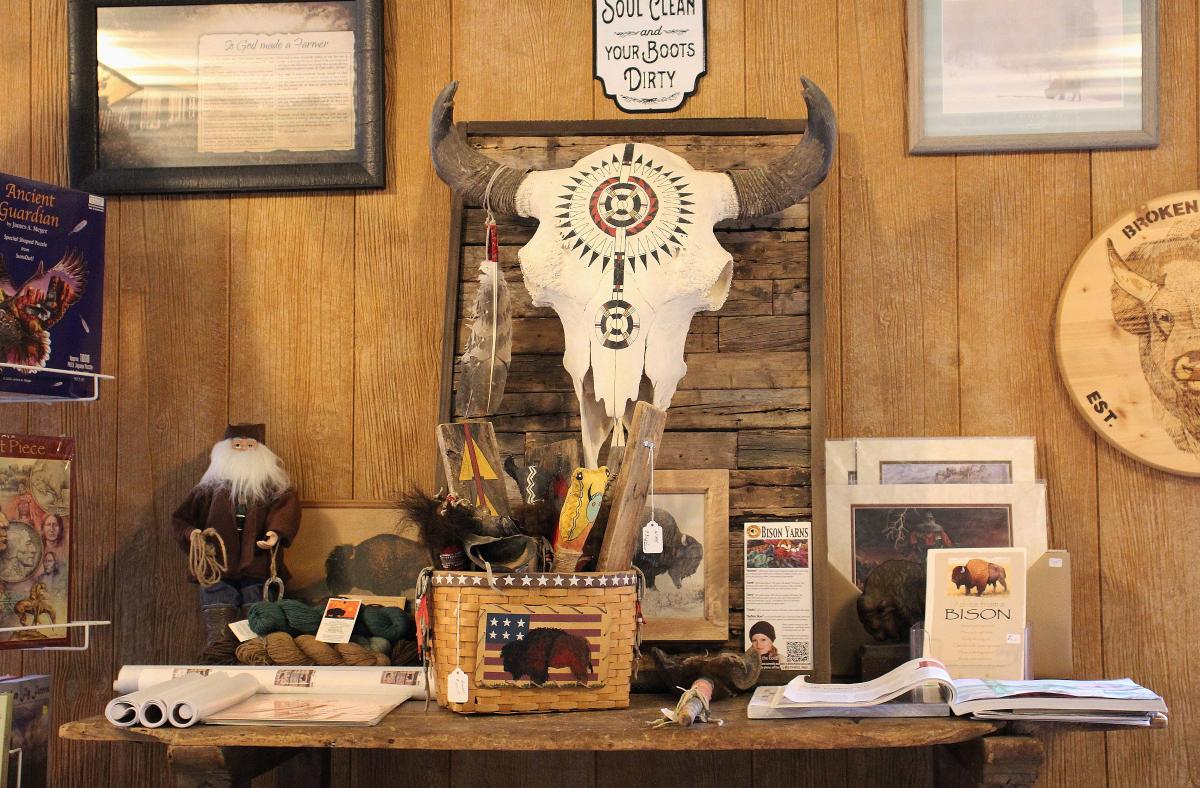 A decorated bison skull hangs on the wall. A table below it holds various bison products.