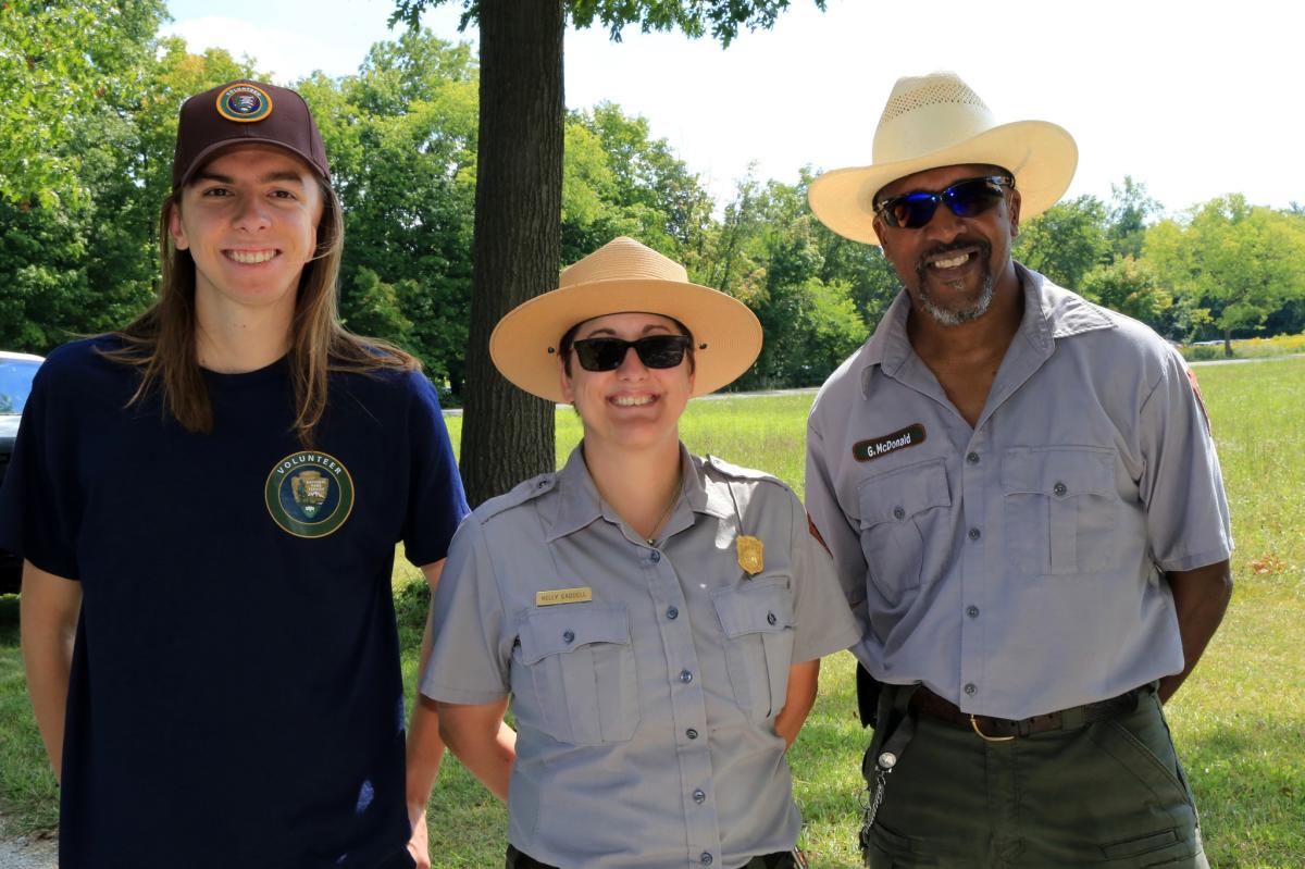 Two park rangers and a park volunteer stand, smiling at the camera