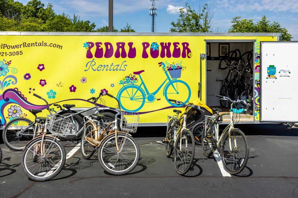 A yellow trailer has an open door with bikes inside. Bikes are set up in front of the trailer.