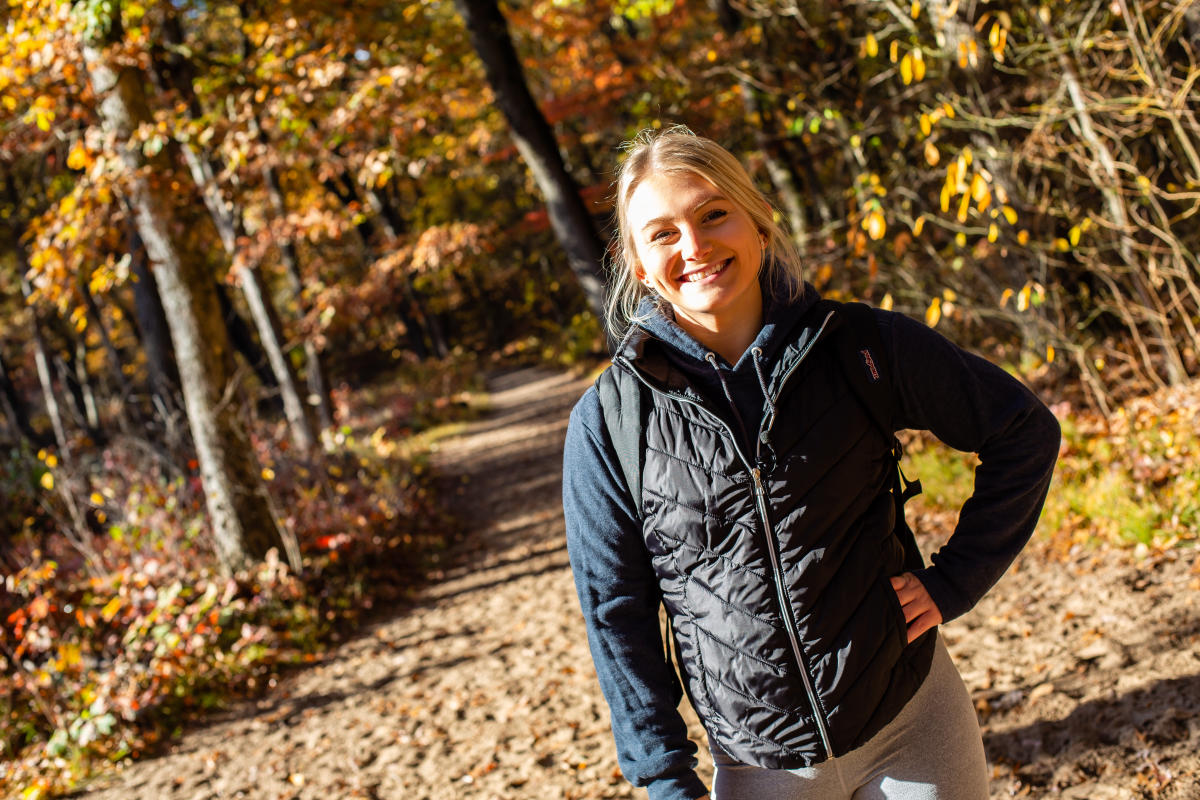 A blonde woman stands on a trail with fall colors