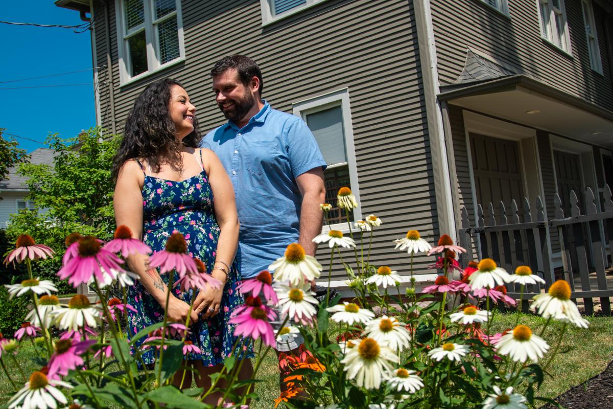 A couple smile at each other in front of white and pink flowers