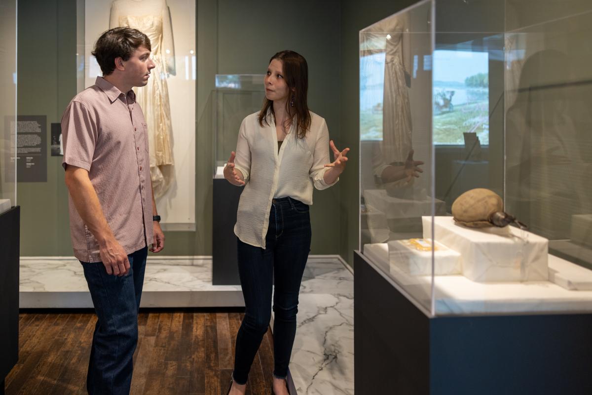 A young woman and man talk to each other in front of a glass museum display