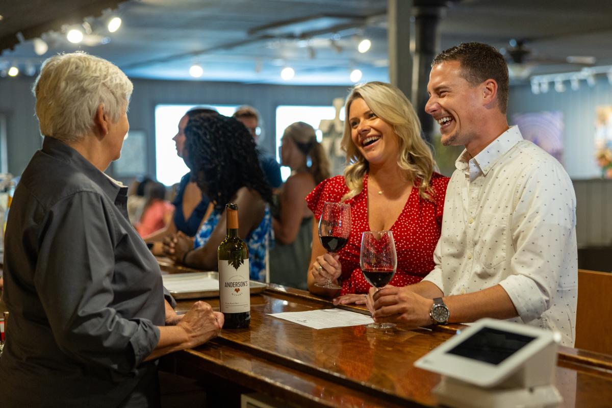 A couple laughs while holding wine glasses at a counter