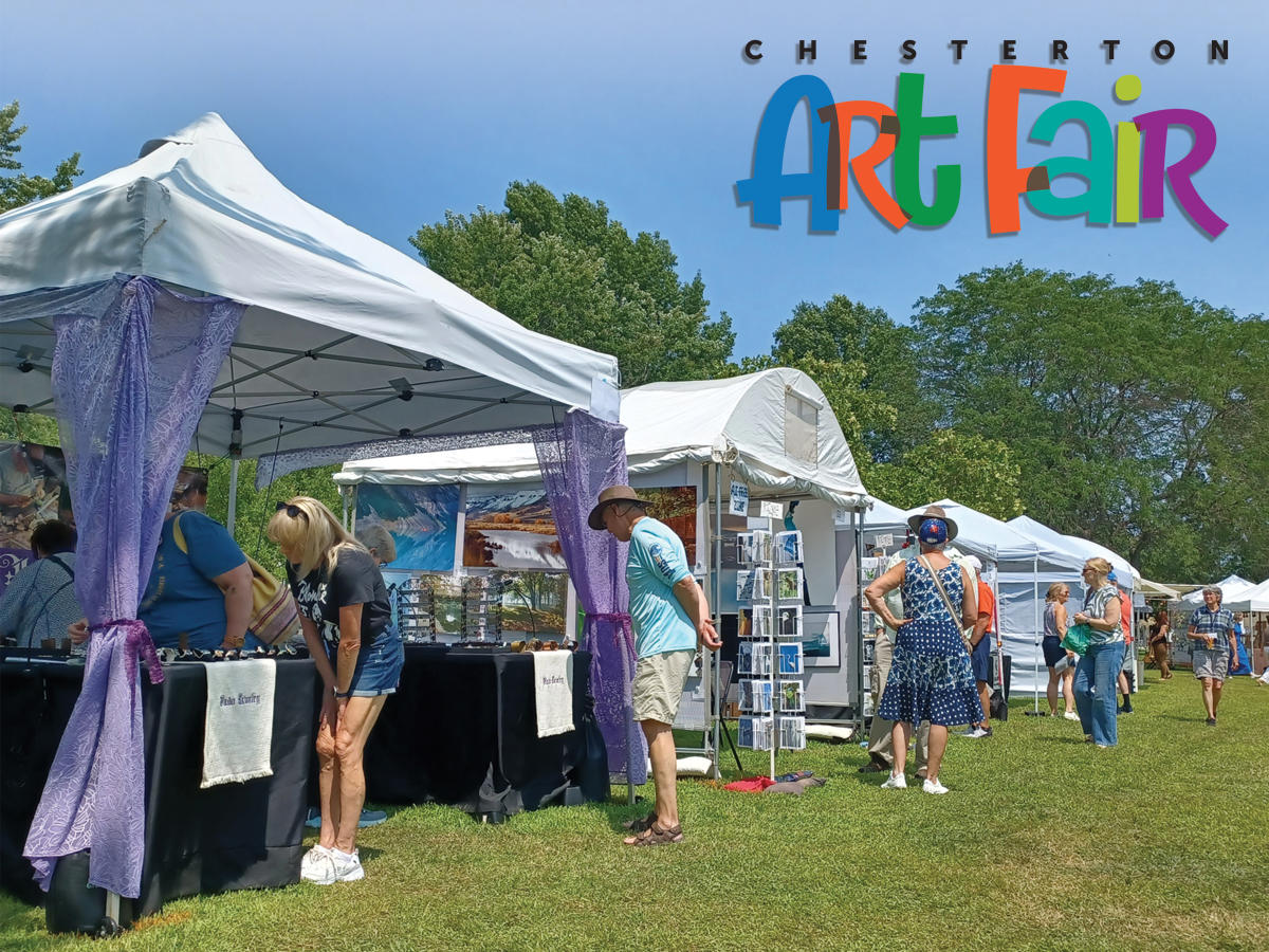 People browse art booths under white tents at an outdoor art fair on a sunny day.