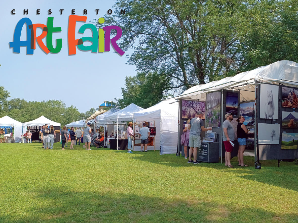 People browse art displayed in white tents at the Chesterton Art Fair on a sunny day.