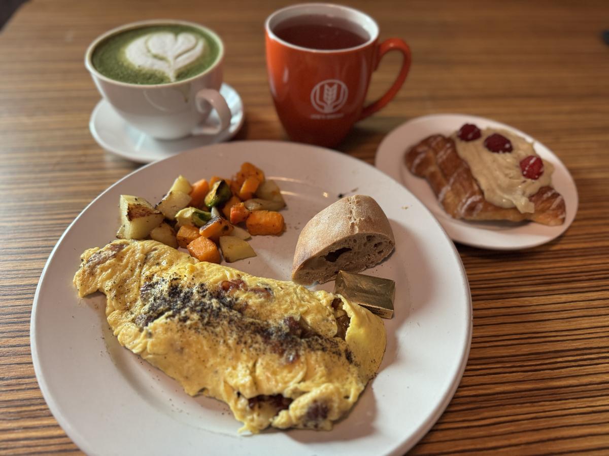 A white plate with an omelet, bread, and vegetables sits in front of a matcha latte, tea, and a pastry with berries and frosting on top.