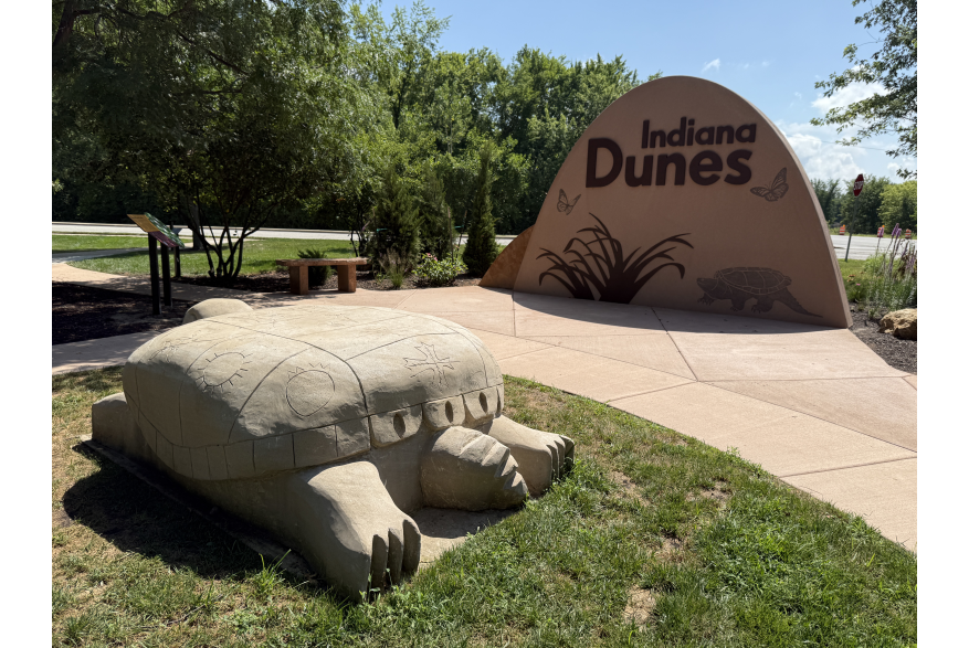A large stone turtle sculpture at the Indiana Dunes Visitor Center, part of the Indigenous Cultural Trail, with a rock engraved with the Indiana Dunes logo in the background.