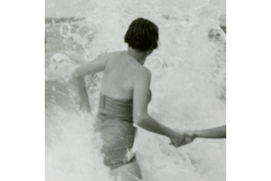 Vintage black-and-white photograph of a person wading through crashing waves while holding another person's hand.