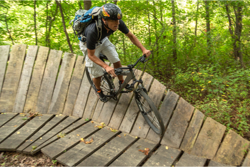 A man wearing a helmet rides a mountain bike on a wooden raised trail