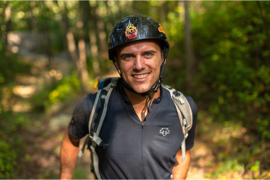 A man in a bike helmet smiles at the camera.