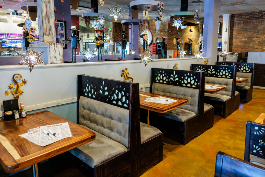Black booths with gray seats  line up along a half wall. Mexican art lines the wall and decorations hang from the ceiling.
