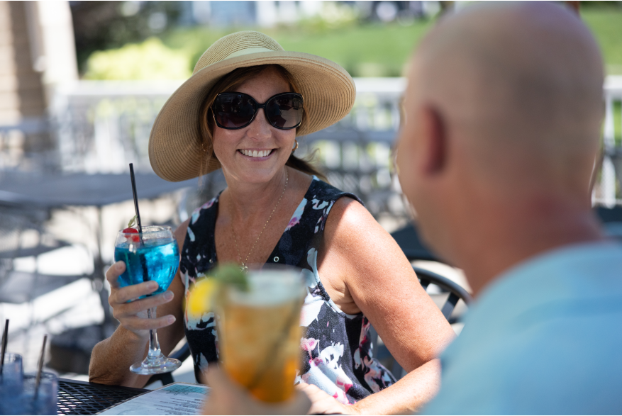 A woman in a hat and sunglasses holds a glass while smiling
