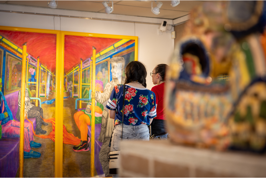 Two people look at a brightly colored painting on the wall. A blurred statue is in the foreground.