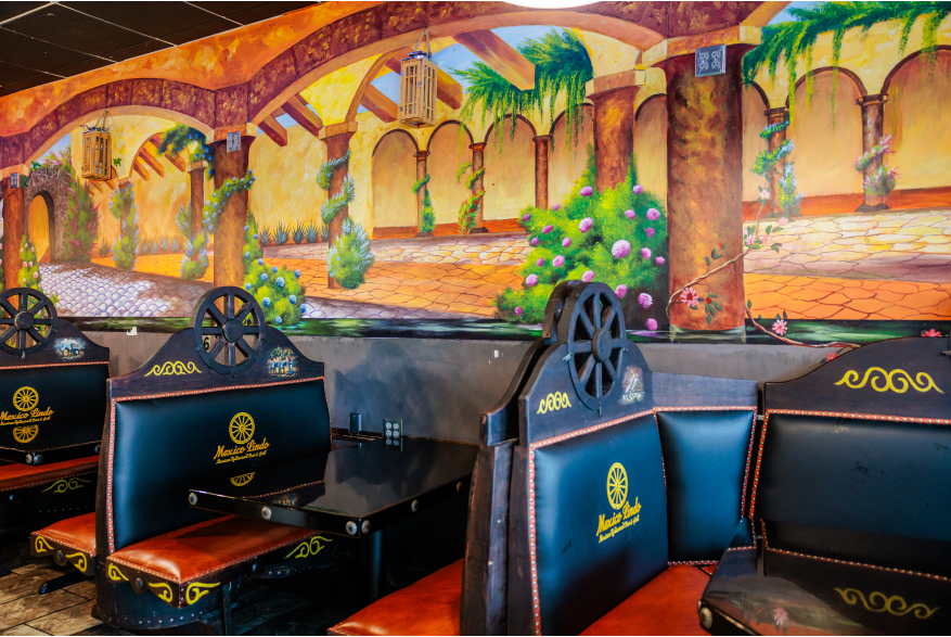 Black stylized booths with wagon wheel decorations line the wall. A mural with a patio building and flowers is on the wall.