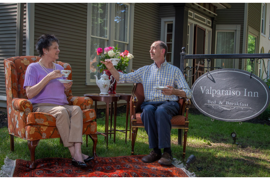 A man and women sit on furniture drinking tea while sitting on the front lawn.