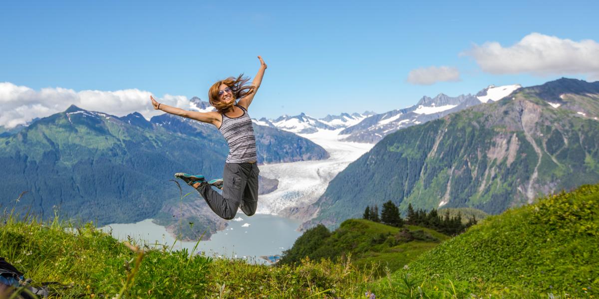 A person jumping for joy with the breathtaking green mountains and blue water in Juneau, AK.