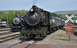 Two historic steam locomotives at Steamtown National Historic Site in Scranton, PA surrounded by tracks and greenery.