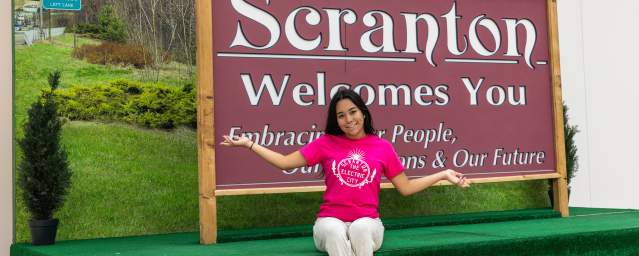 Woman posing for a pic in front of the Scranton Welcomes You Sign in Downtown Scranton, PA