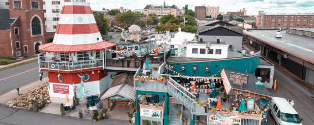 Colorful Cooper's Seafood House restaurant with a lighthouse design, featuring outdoor seating, decorations, and a large octopus sculpture nearby.