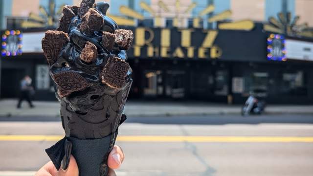 A black soft-serve cone from Black Cow Cookies & Cream, topped with chocolate sandwich cookies, is held outside The Ritz Theater in Downtown Scranton, PA.