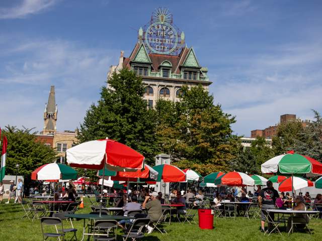 Tables with Italian-colored umbrellas in Courthouse Square in front of the Electric City Sign