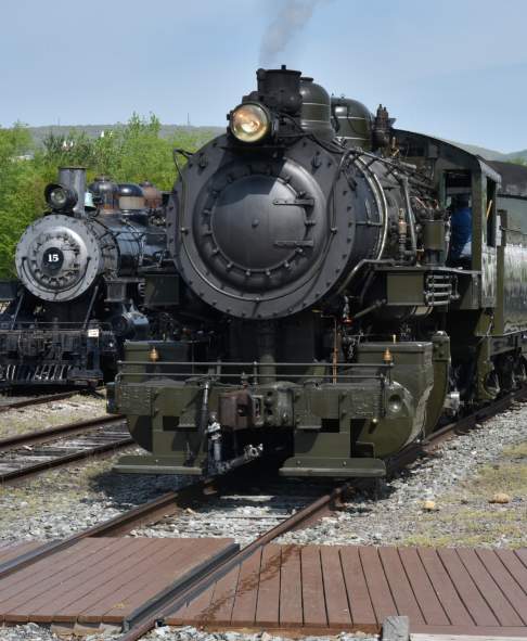 Two historic steam locomotives at Steamtown National Historic Site in Scranton, PA surrounded by tracks and greenery.