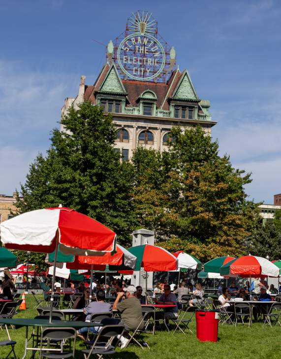 Tables with Italian-colored umbrellas in Courthouse Square in front of the Electric City Sign