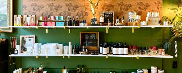 Boutique display with skincare, wellness products, and artisan goods on white shelves against a green wall with buffalo-print wallpaper and gold antelope decor at Tusk in downtown Scranton.